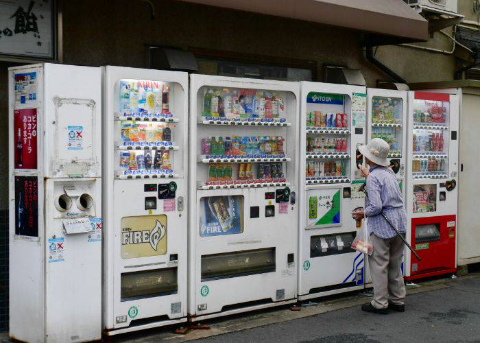 An old lady in Japan, browsing the drinks at a vending machine.